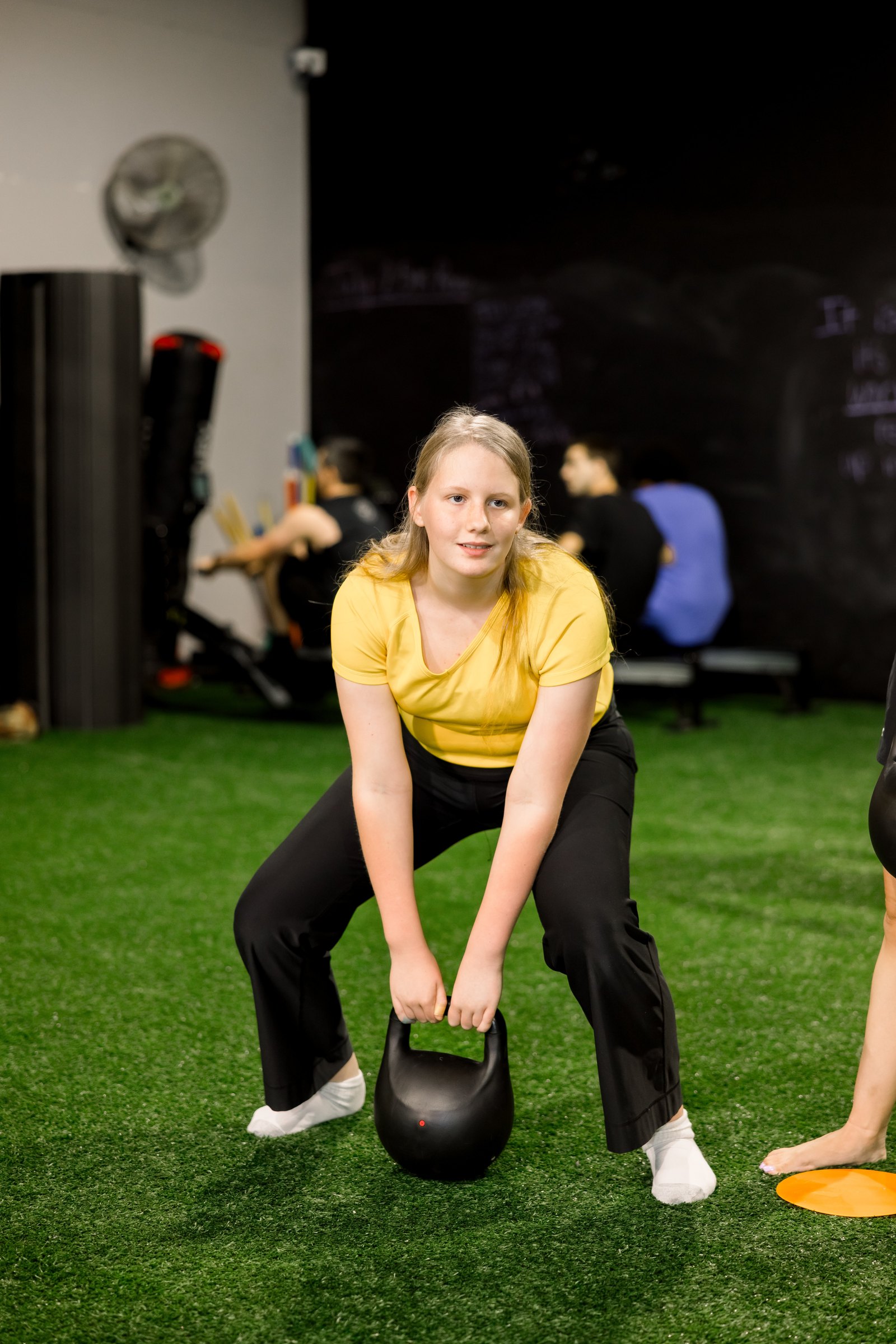 An athlete in a yellow shirt sets up a kettlebell deadlift on the turf