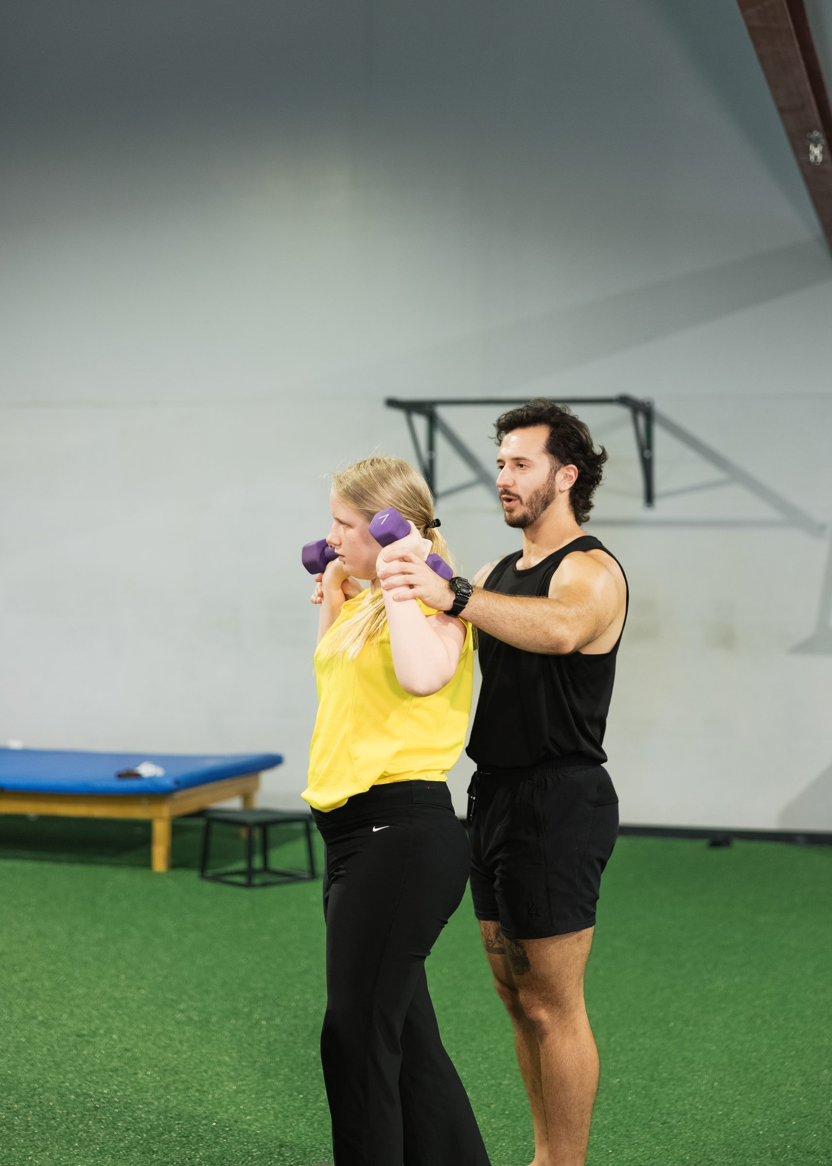 A coach guiding his athlete through a dumbbell press