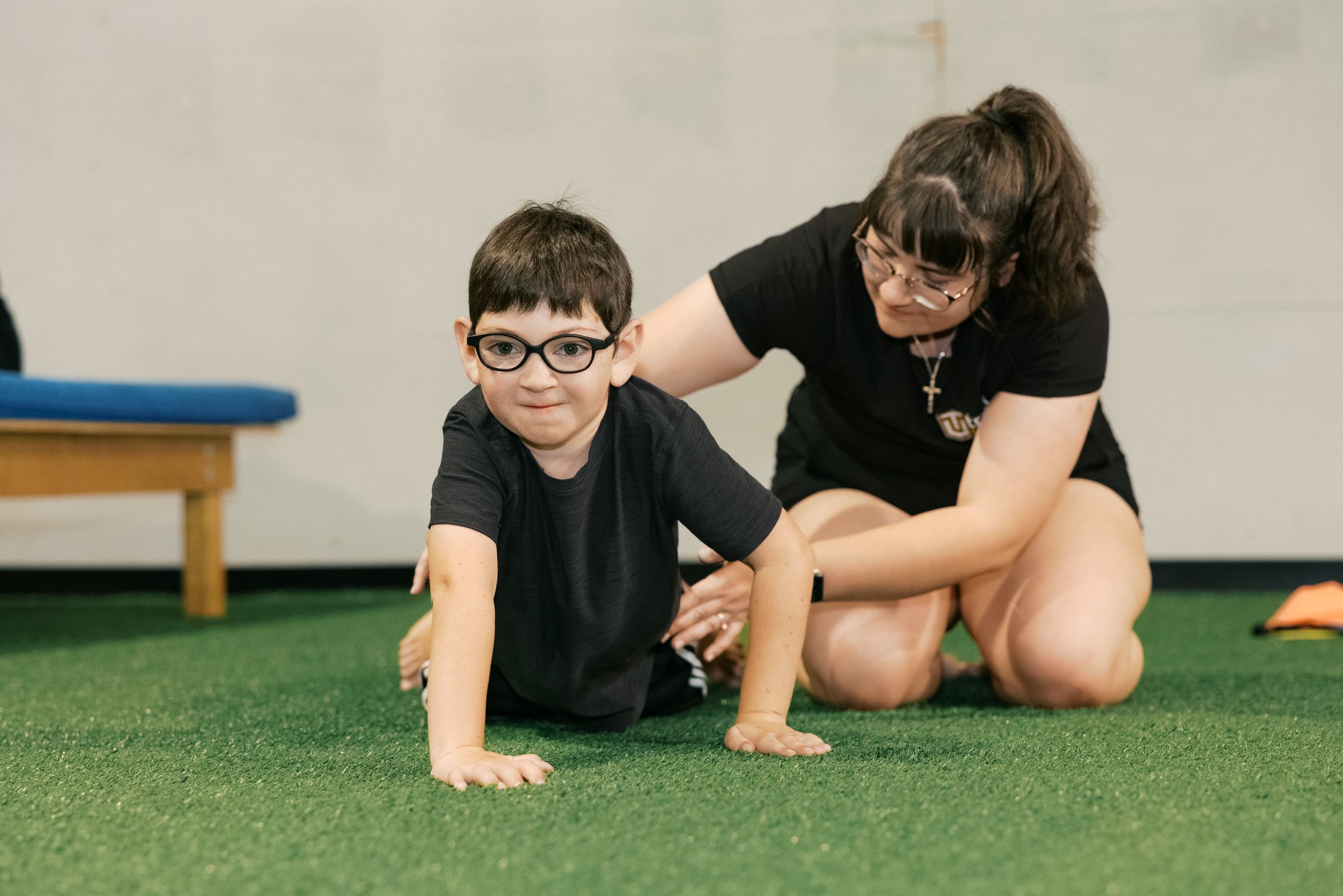 A young athlete bear-crawling with his coach low beside him
