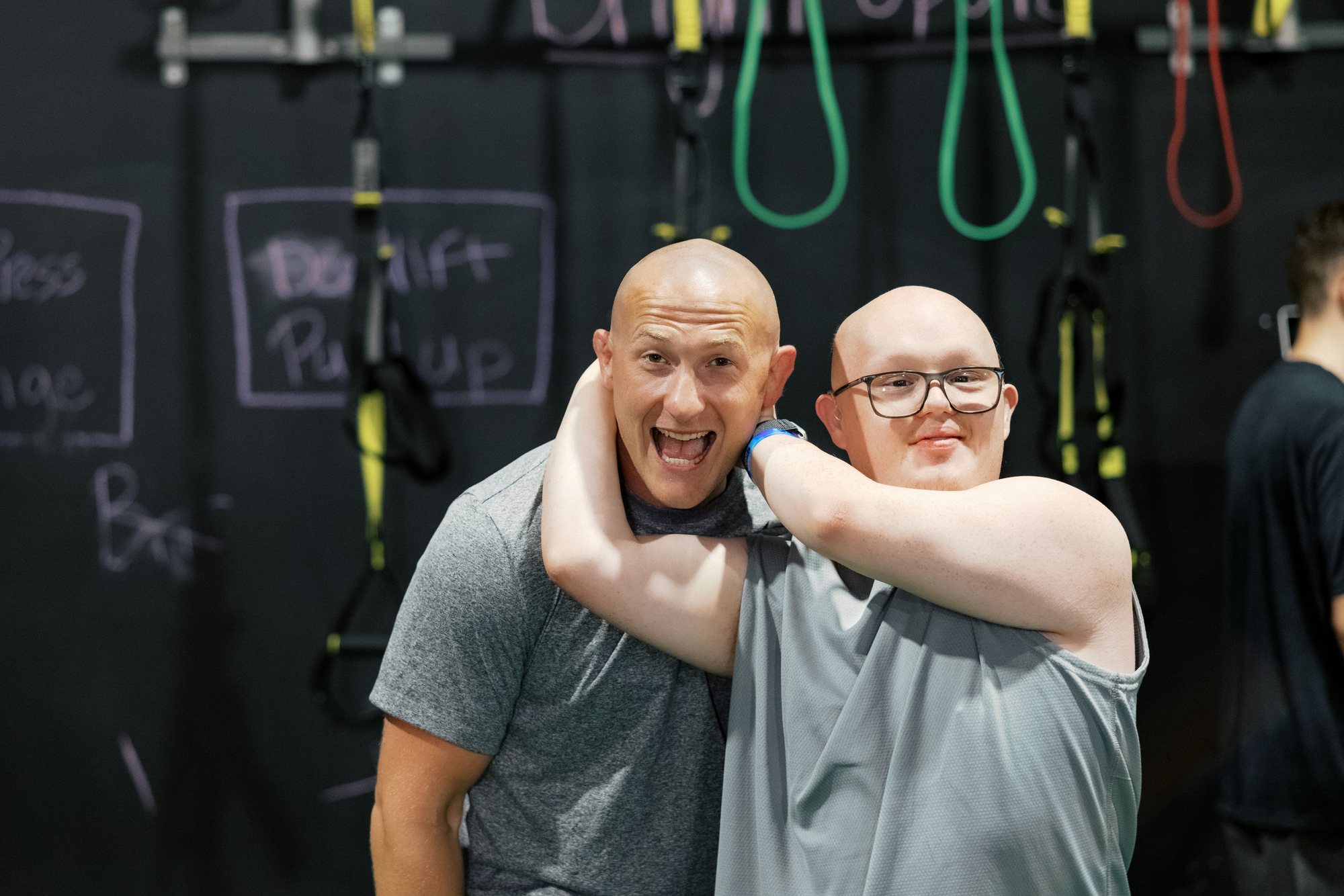 An athlete in glasses hooks an arm around Damon Vincent's neck; Damon is laughing and the athlete is smiling